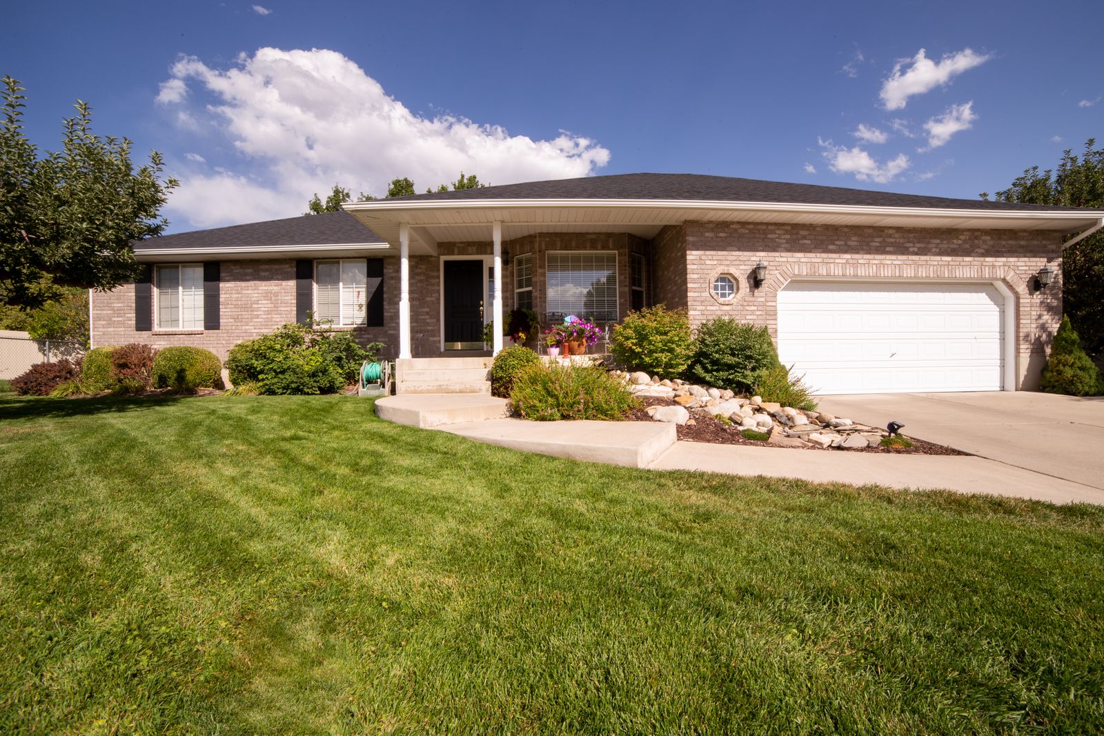 A brick house with a front lawn, shrubs, and a driveway